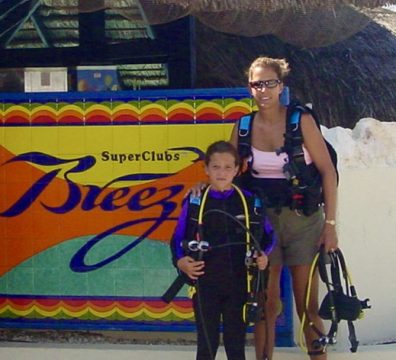 A woman and child in scuba gear standing next to a sign.